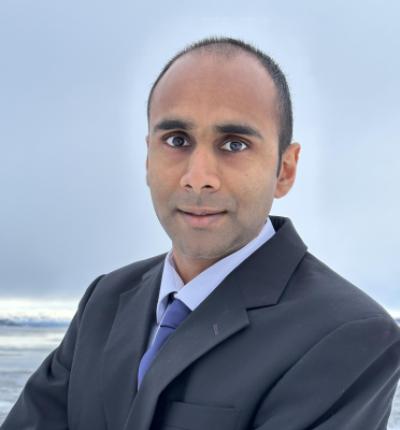 A man wearing a dark colored suit and tie superimposed in front of crashing arctic beach waves