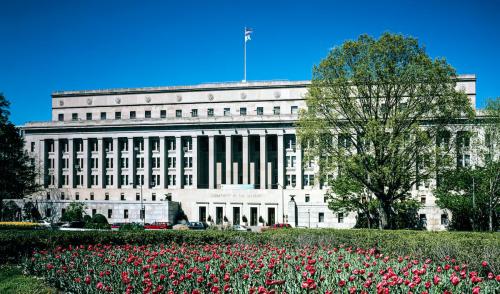 The main interior building against a blue sky. A large tree occupies the right side, and a flower bed of red tulips dominates the foreground of the photo.