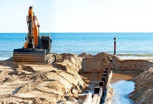 An excavator on top of a pile of sand near the ocean