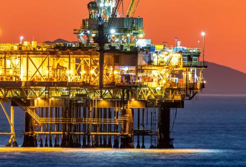 Offshore oil platform off the coast of California against a moody, orange sky as the sun sets behind the rig.
