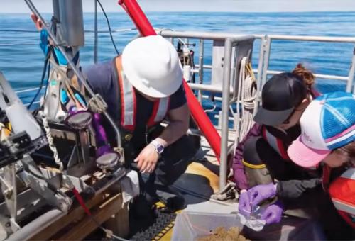 Close up of three people on a ship in the ocean taking samples of dirt from the sea floor