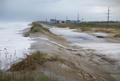 Ocean waves during a storm washing over a small sand dune onto a nearby road