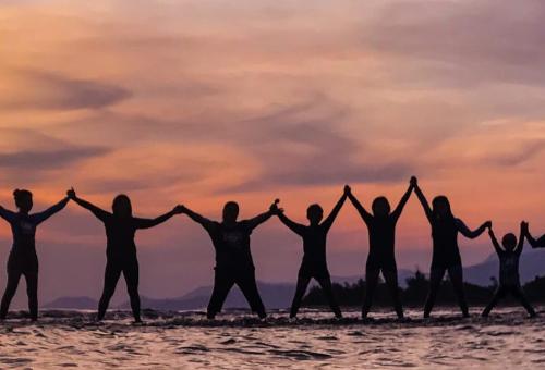 Silhouettes of 21 people standing in ankle deep water, holding hands like paper dolls